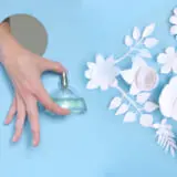 A woman's hand looks out of the hole and holds a bottle of perfume