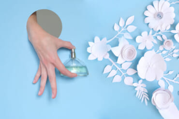 A woman's hand looks out of the hole and holds a bottle of perfume