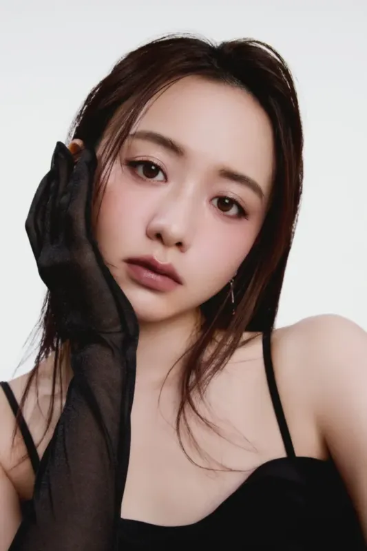 黒い手袋をつけた女性のポートレート。女性はカメラを見ており、白い背景に黒いキャミソールを着ている。