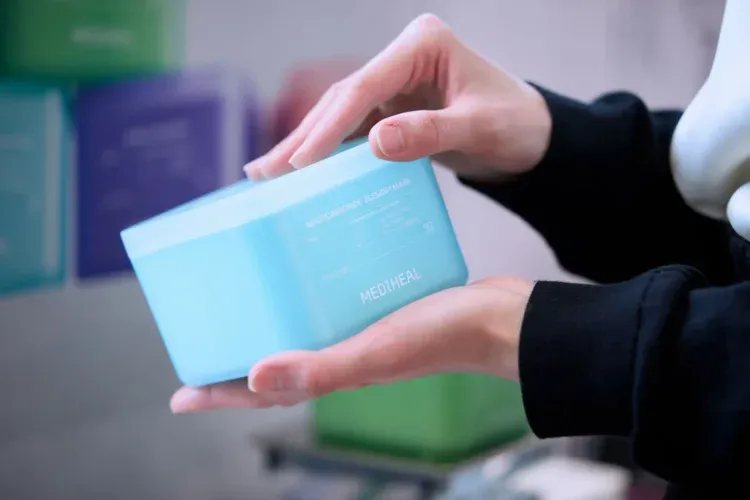 水色の容器に入ったフェイスパックを手に持っている様子。