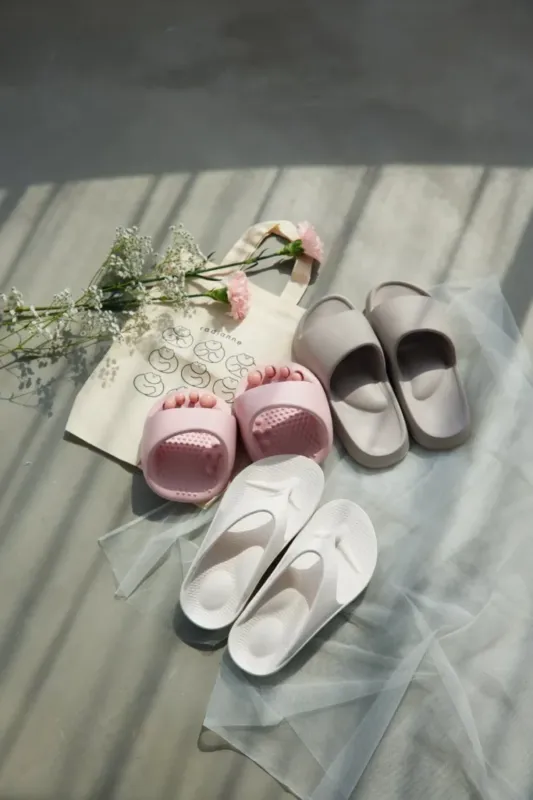 さまざまなサンダルが置かれた写真。ピンクのサンダル、グレーのサンダル、白いサンダル、トートバッグ、花が写っています。